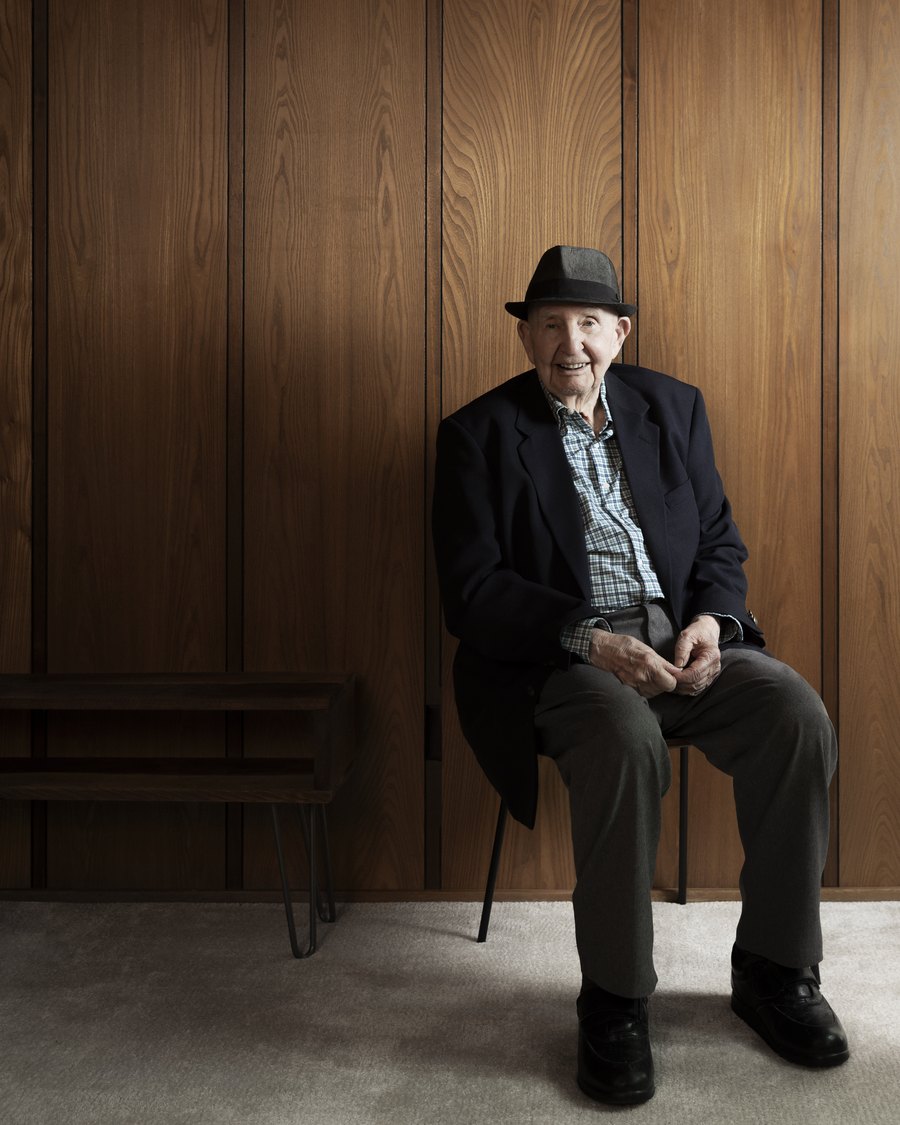Bob Rummer in a hat and jacket, seated against a walnut-panelled wall.